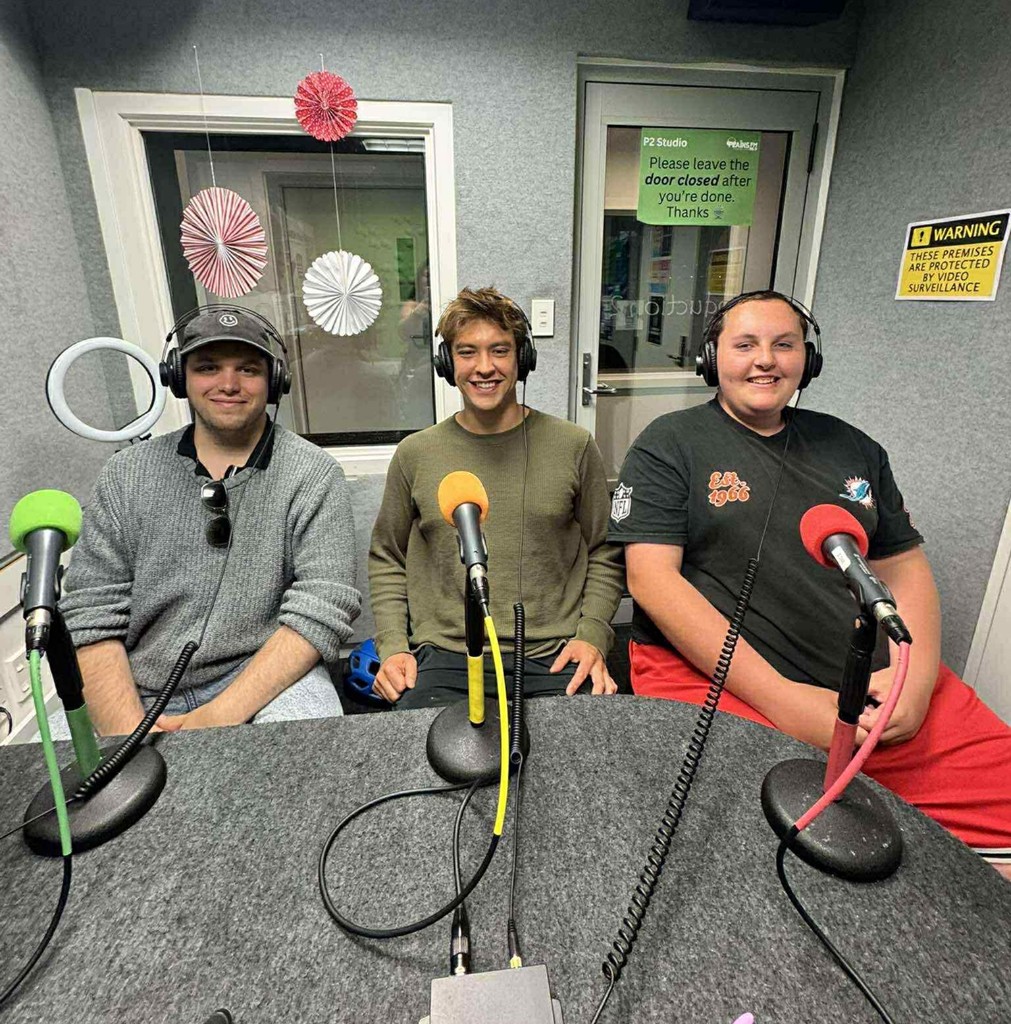 Juniper, Kane, and Max wearing headphones at microphones in a studio.